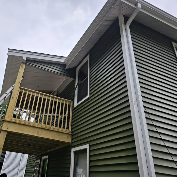 New green vinyl siding with white trim and gutter beside a wood porch