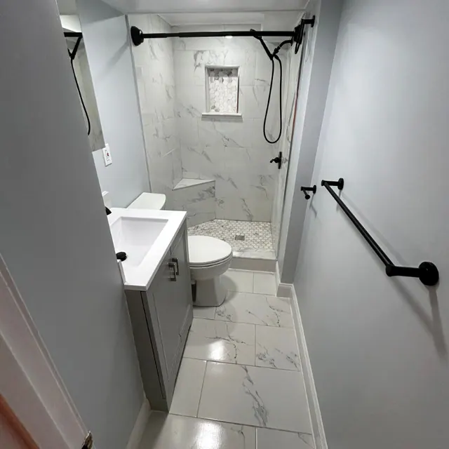 Remodeled bathroom in marble-look tile with matte black fixtures, grab bar and a walk-in shower