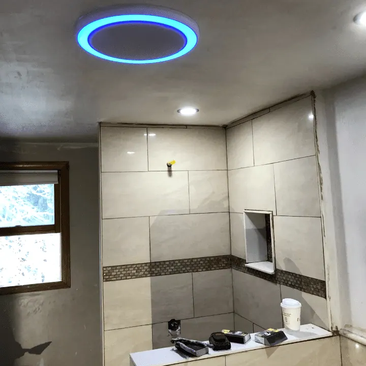 Tiled shower with a mosaic band and niche under a lit ring-light fan