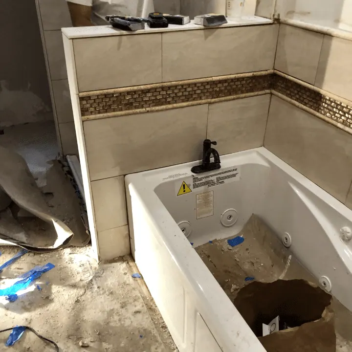 New soaking tub with a tiled surround and a mosaic accent band, mid-install