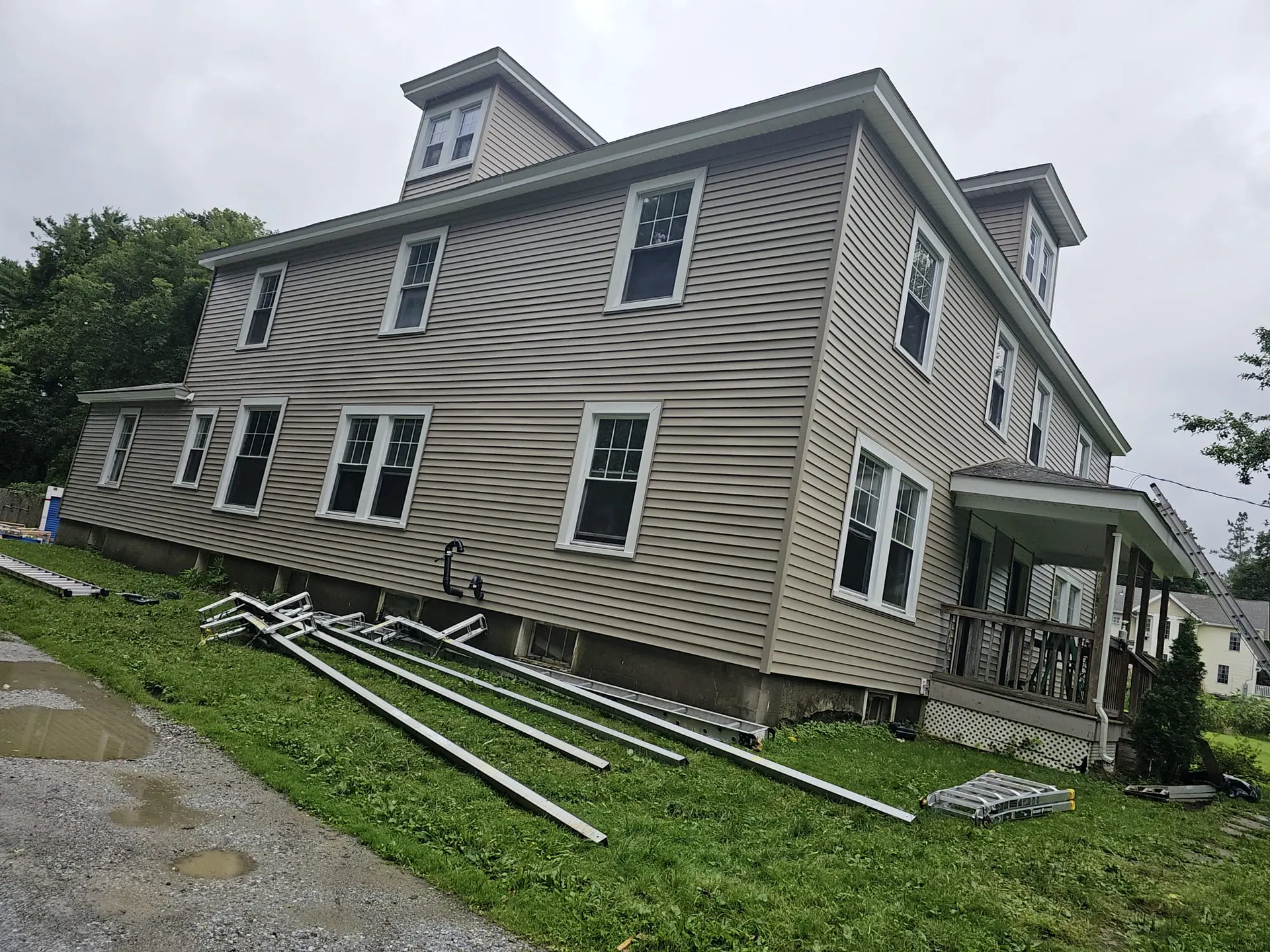 Large colonial house getting new tan vinyl siding, siding materials laid out on the lawn