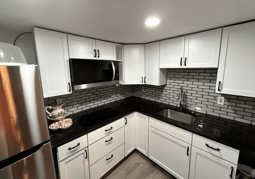 Remodeled kitchen with white shaker cabinets, black granite counters, gray subway backsplash and stainless appliances